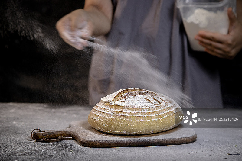 面包师在手工酸面包上洒面粉图片素材