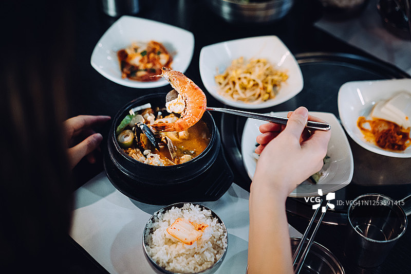 在肩膀上的年轻亚洲女人享受新鲜的传统韩式海鲜豆腐汤米饭和各种开胃菜在韩国餐厅图片素材