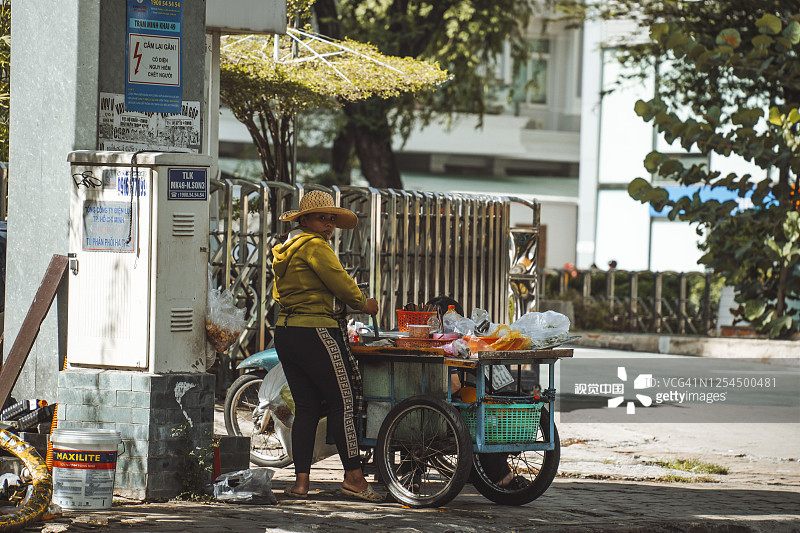 西贡(胡志明市)的街道上，妇女推着手推车在人行道上吃早餐图片素材