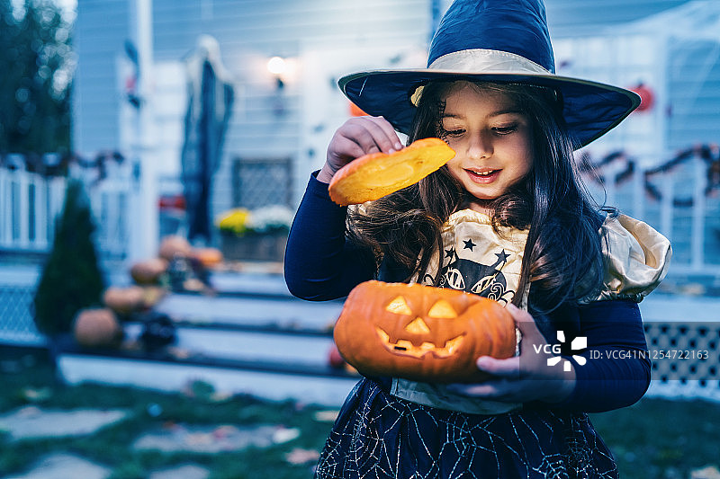 在万圣节不给糖就捣乱的时候，穿着女巫服装的小女孩拿着南瓜灯图片素材