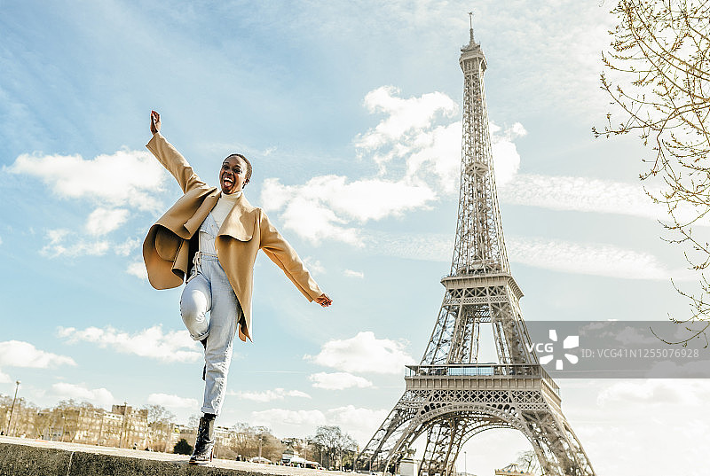 法国巴黎，一名兴奋的女子从以埃菲尔铁塔为背景的挡土墙上跳下图片素材