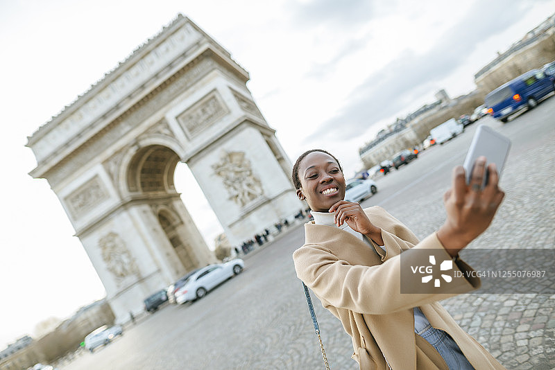 快乐的年轻女子与凯旋门自拍，巴黎，法国图片素材