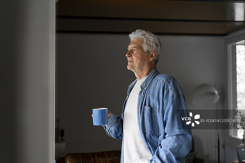体贴的老人拿着咖啡杯，从家里的窗户往外看图片素材
