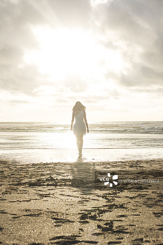 一个年轻的女人在日落的时候在海滩上散步图片素材