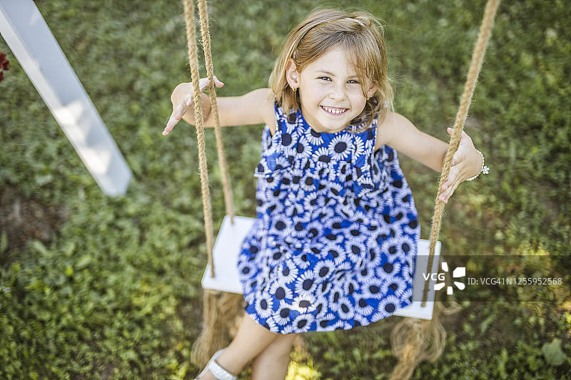 一个快乐的小女孩坐在秋千上，面带微笑图片素材