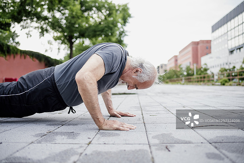 活跃的老年人在城市的人行道上做俯卧撑图片素材