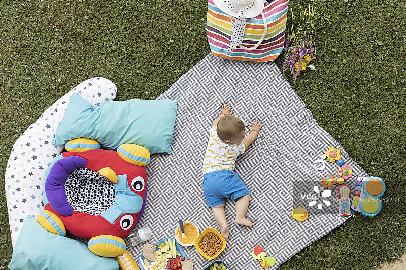 婴儿躺在绿草地上的毯子上。从上面的照片。上面的观点。图片素材