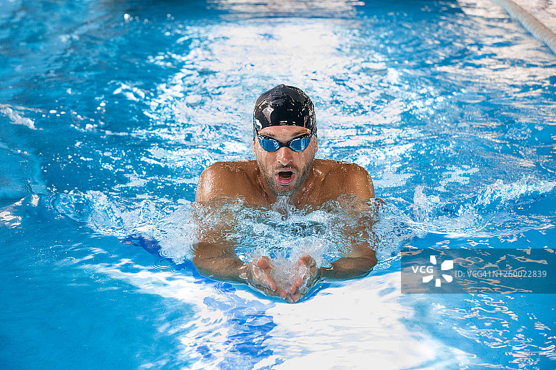 运动中男性游泳运动员在泳池中游泳，蛙泳。前视图，技术游泳。图片素材