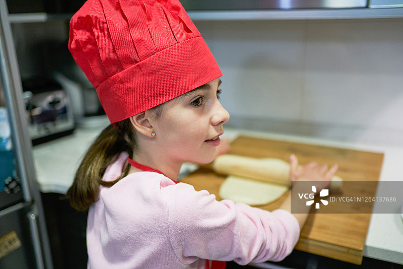 戴着红色厨师帽的女孩用擀面杖擀披萨面团图片素材