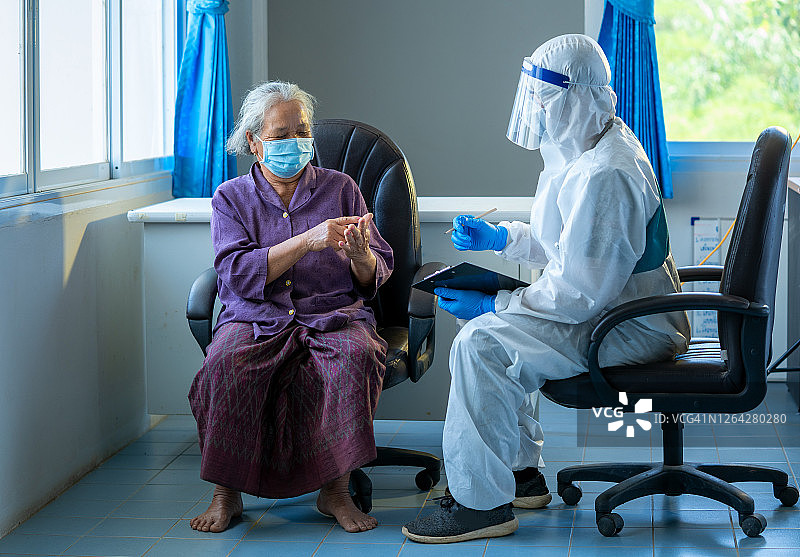 医生在医院检查并询问戴口罩的亚洲老年妇女病人。图片素材