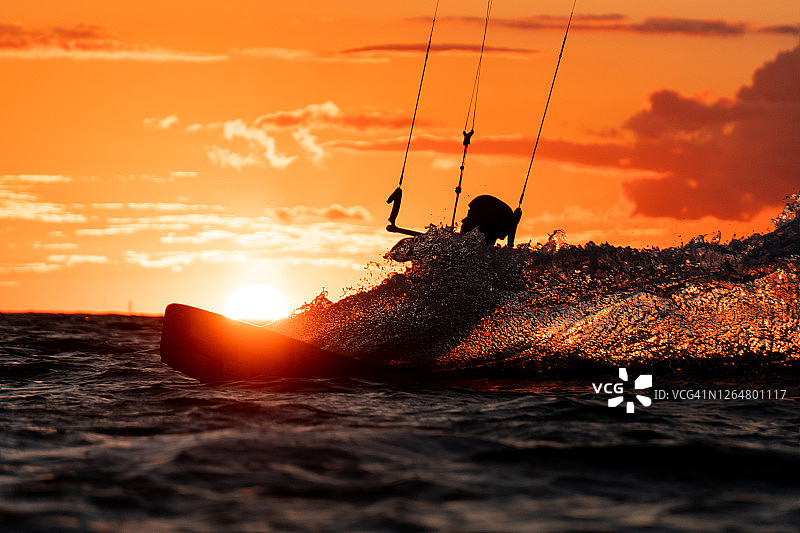 风筝冲浪者的剪影在美丽的橙色日落与太阳的右后方图片素材