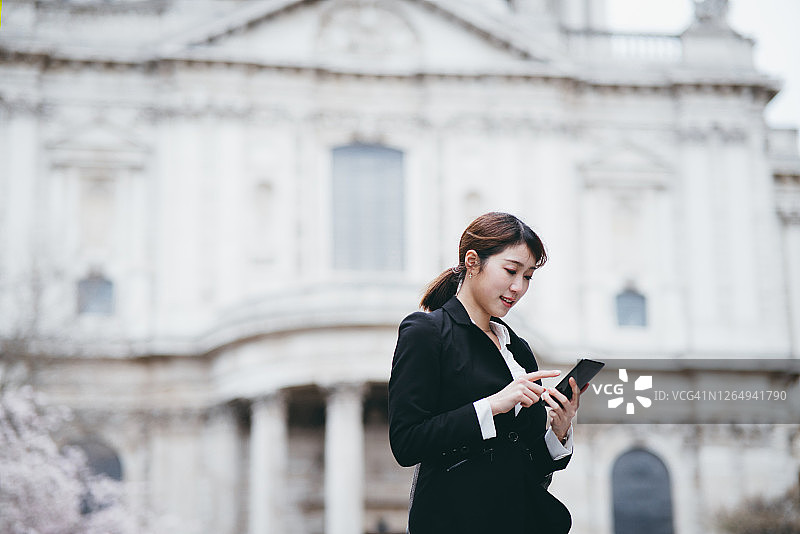 动态业务的概念。成功而自信的年轻亚洲女商人在伦敦市中心散步时用智能手机查看商业计划图片素材