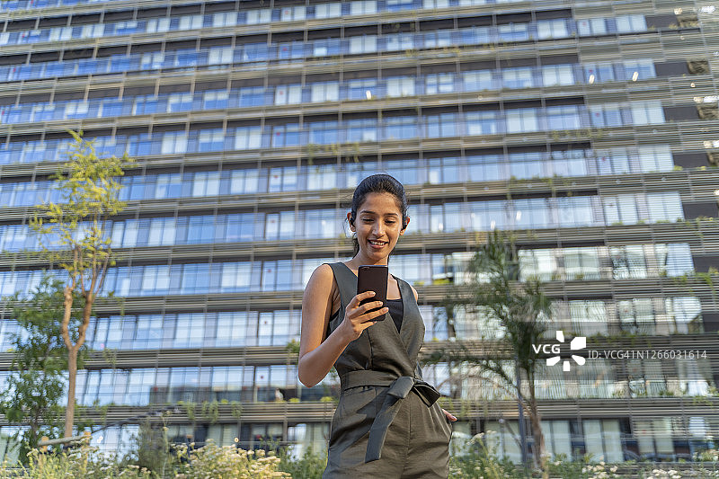 在城市中，女商人站在建筑物前使用手机图片素材