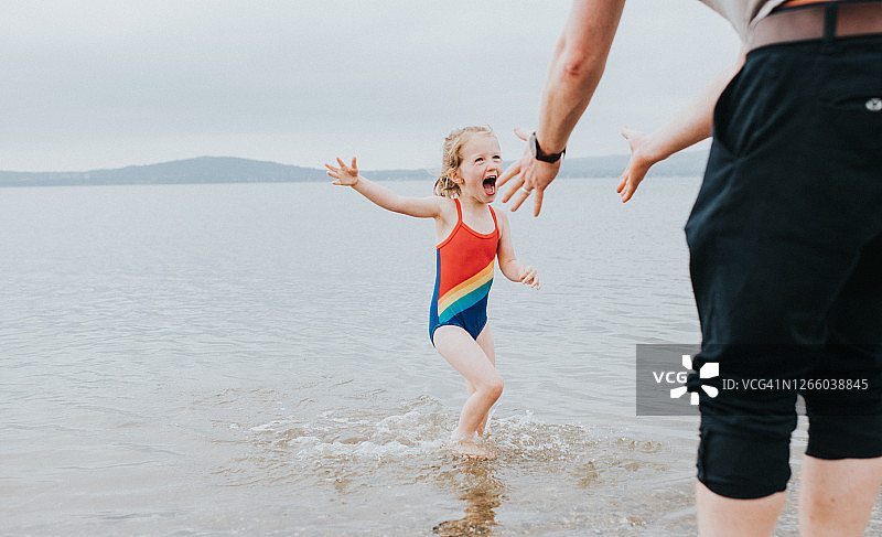 快乐的小女孩在海里划船，穿着游泳衣跑向爸爸图片素材