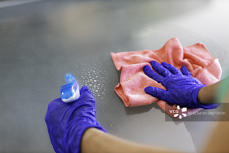 表消毒。清洁表面。女士戴着手套和消毒剂擦拭桌子，以防止细菌和细菌感染图片素材