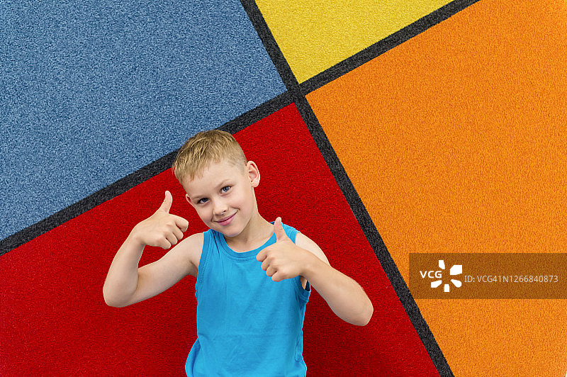 可爱的小男孩在彩色的背景上竖起大拇指。兴奋的孩子在游戏中心玩得很开心。图片素材