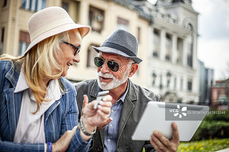 两个老人在网上购物用数字平板电脑-快乐的老年夫妇坐在城市散步和网上购物图片素材