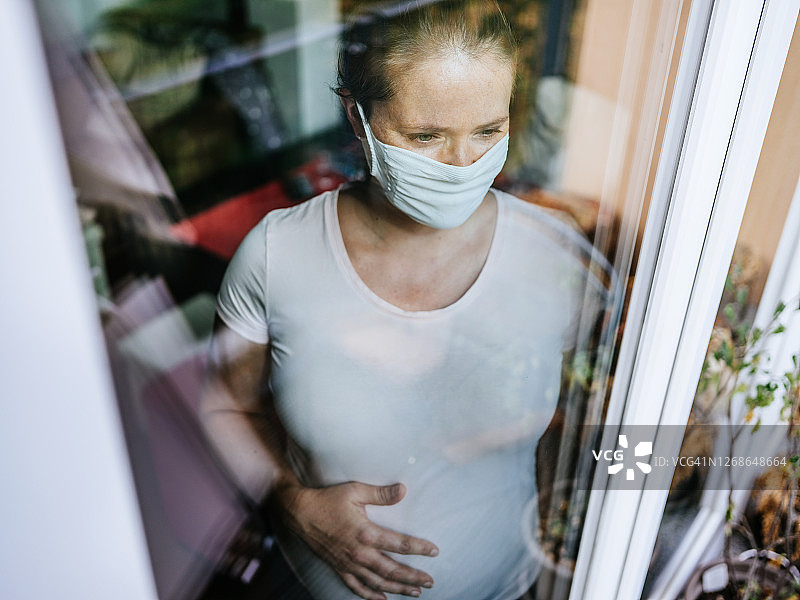 戴口罩的孕妇向窗外看。图片素材
