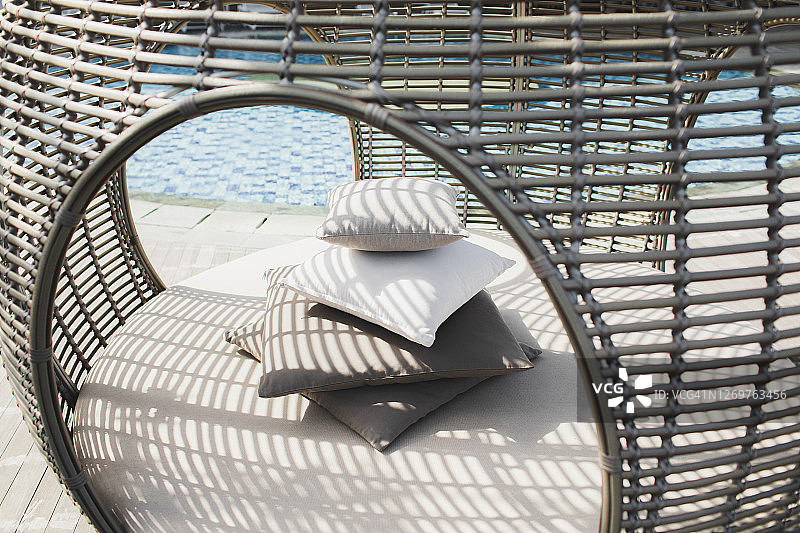 户外现代躺椅上的一堆枕头。美丽的条纹阳光。泳池边的柳条藤条家具。白色和灰色。图片素材