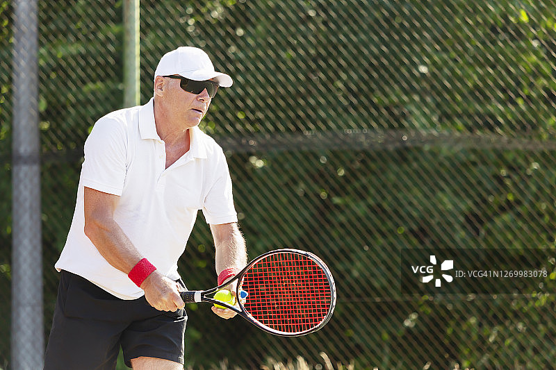 一个上了年纪的网球运动员在户外球场上打网球的特写图片素材