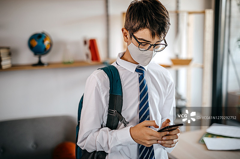 十几岁的男孩使用手机戴着防护口罩在学校制服图片素材