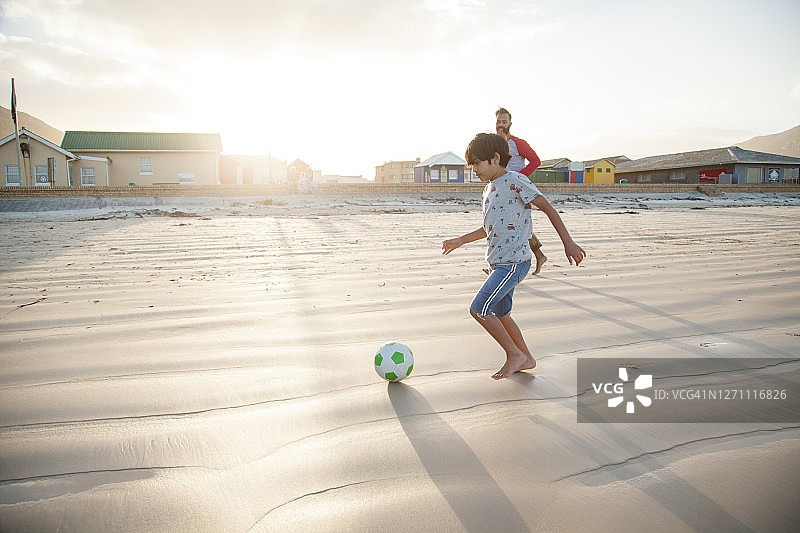 日落时分，父亲和儿子在沙滩上踢足球图片素材