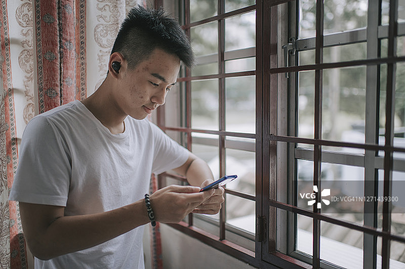 亚洲华人少年在家里用蓝牙耳机和智能手机听音乐图片素材