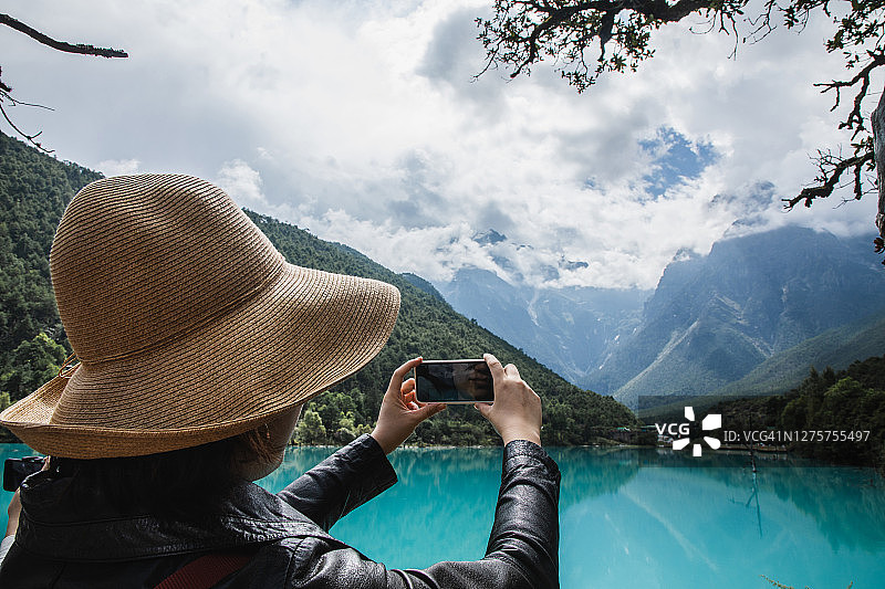 一名女子用智能手机拍摄美丽的风景(雪山和美丽的湖泊)图片素材