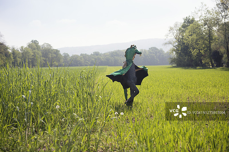 穿着绿色龙装的女孩(6-7岁)在绿树成荫的田野里玩耍图片素材
