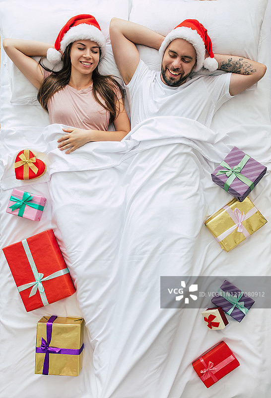 俯视图完整的照片美丽的年轻幸福的夫妇在圣诞帽与许多圣诞礼物盒和梦想而睡觉。上面的照片。圣诞快乐，恭贺新禧图片素材