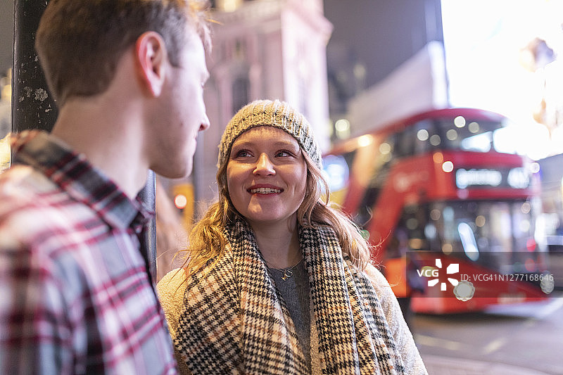 一对年轻夫妇站在皮卡迪利广场上聊天，背景是一辆双层巴士图片素材