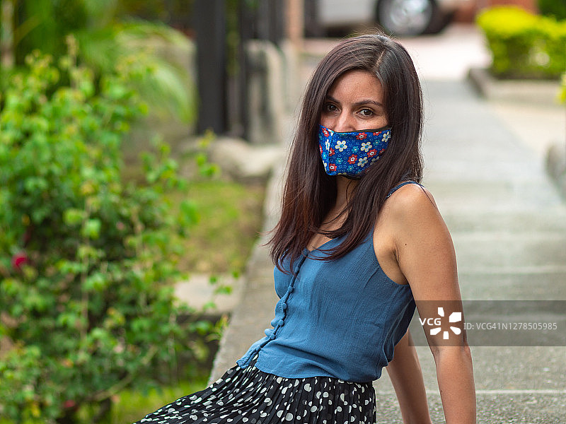 西班牙裔年轻女子坐在人行道上，戴着蓝花手工面膜图片素材