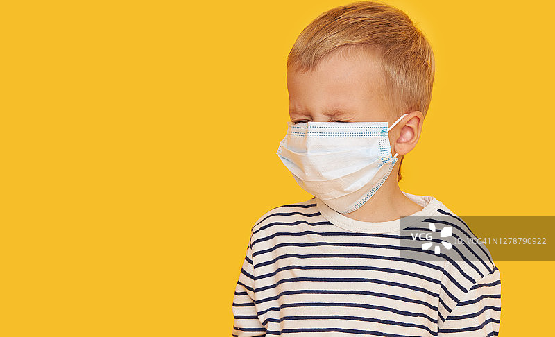 一个生病的小男孩的肖像戴着保护面具在黄色的背景。新冠肺炎大流行期间的病毒防护和保健理念图片素材