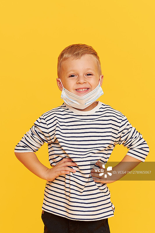 可爱的小男孩的肖像戴着保护面具在黄色的背景。新冠肺炎大流行期间的病毒防护和保健理念图片素材