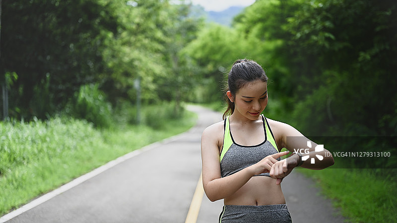 年轻女性在公园慢跑前设置智能手表。图片素材