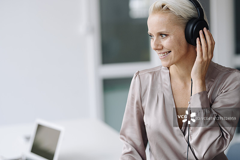 微笑的女商人戴着耳机听着音乐坐在办公室里看向别处图片素材