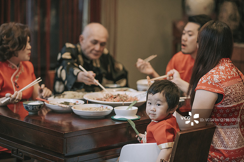 亚洲中国男婴看着镜头，家人在吃年夜饭吃传统菜肴图片素材