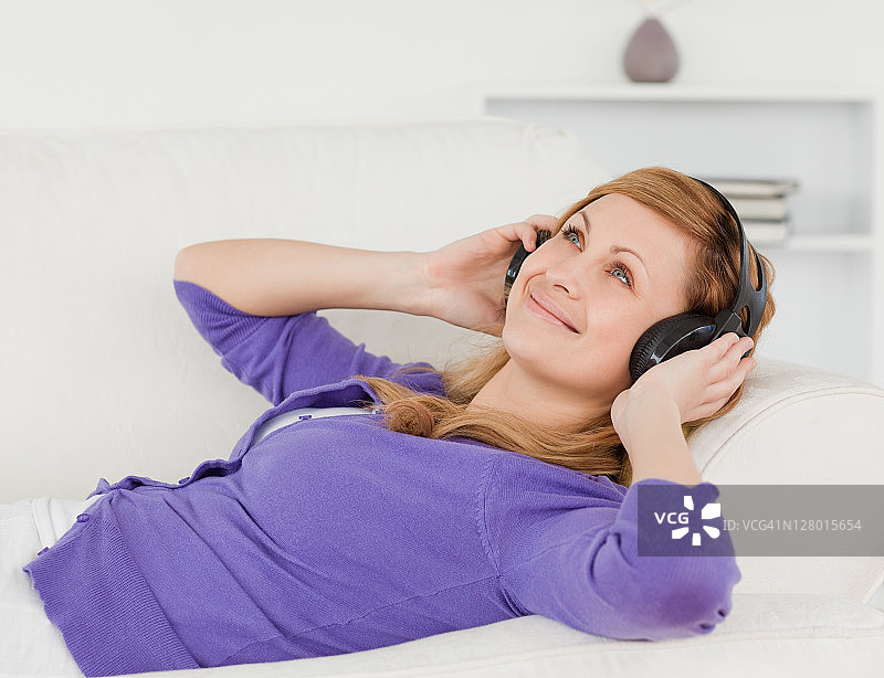 美丽的红发女人躺在沙发上听音乐，享受这一刻图片素材
