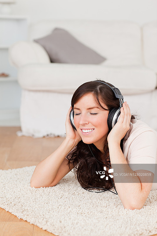 漂亮的黑发女人躺在地毯上戴耳机图片素材