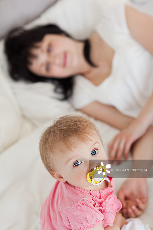 可爱的宝宝看着镜头，妈妈正躺在床上图片素材