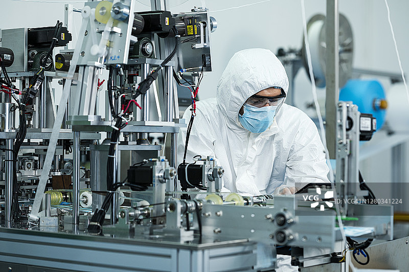 技术人员在口罩工厂检查产品质量。他在自动化机器生产线上工作时使用数码平板电脑。图片素材