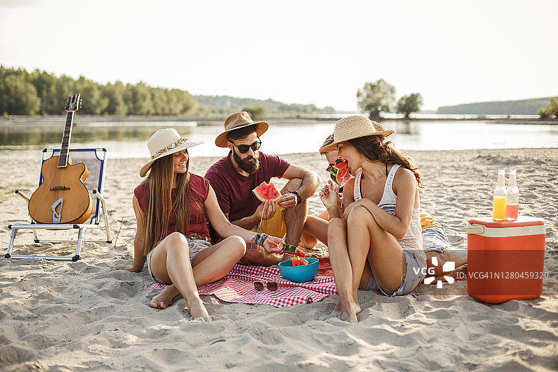 一群年轻人在海滩野餐时享用新鲜的西瓜图片素材