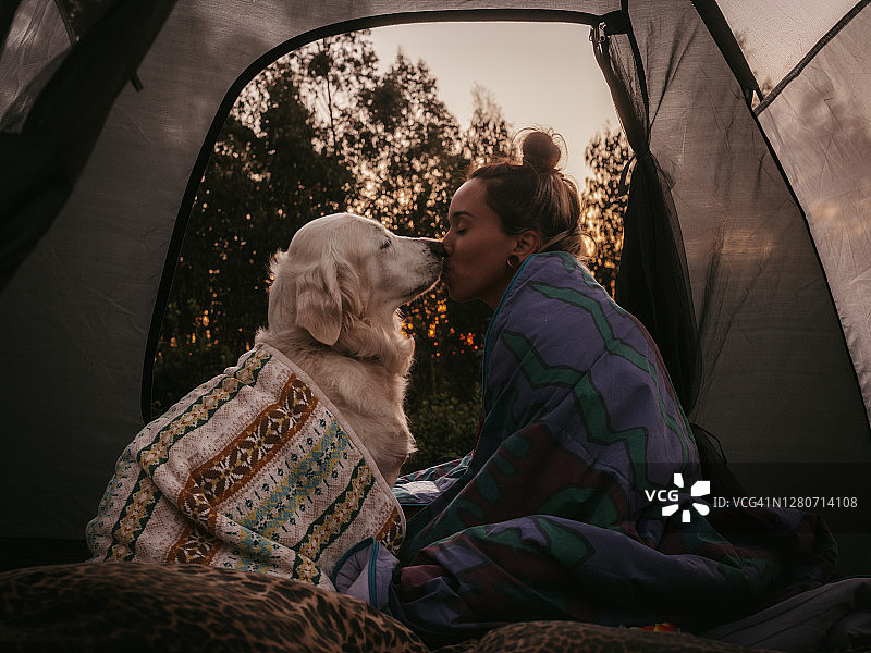 年轻女子和她的狗在大自然的帐篷，日落图片素材