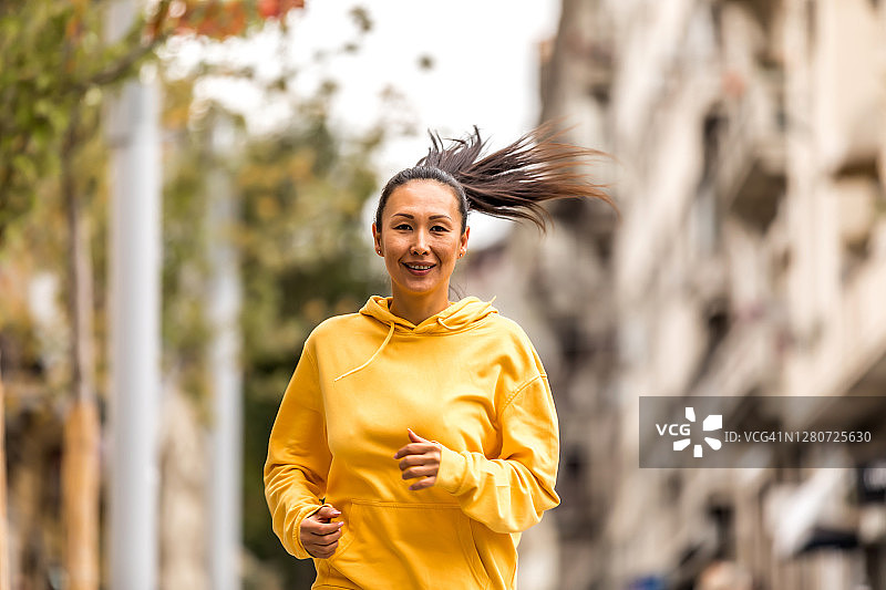 成熟的女运动员在城市郊区的秋日街道上快速奔跑。图片素材