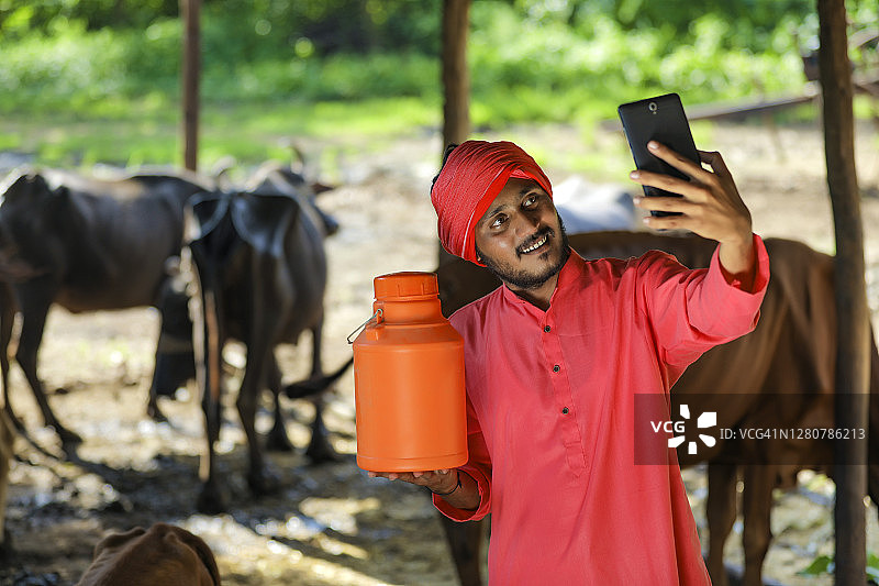 印度农民拿着奶瓶用智能手机自拍图片素材