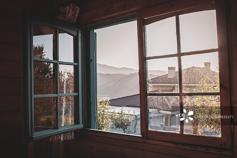 在乡下的房子里开着玻璃脏的窗户。从窗口看山。乡村建筑的内部。村庄的架构。秋天在山村。阳光透过开着的窗户。图片素材