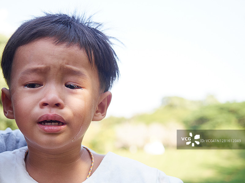 一个亚洲男孩在公园里站起来时，脸上流泪。关闭了。图片素材