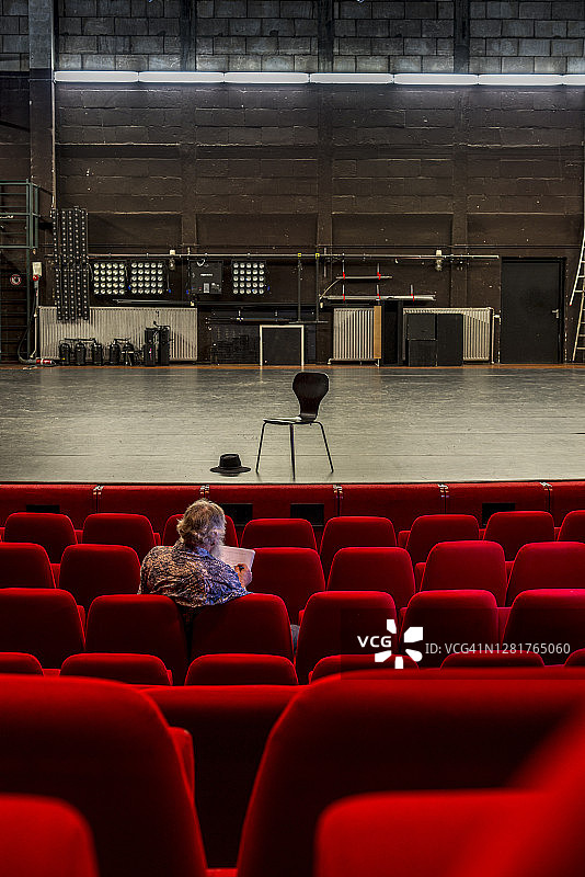 导演在空荡荡的剧院里写剧本，有红椅子和空荡荡的舞台图片素材