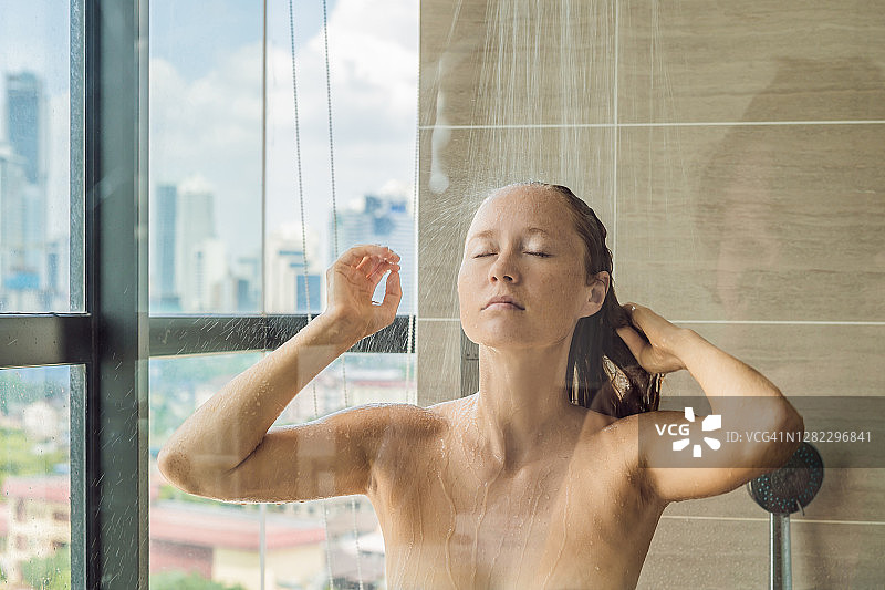 美丽的女人在淋浴后的玻璃与滴在一个窗口的背景与城市的全景图片素材