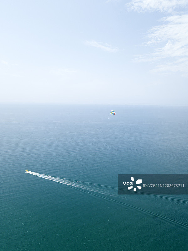 鸟瞰图的人与降落伞飞行在绿松石蓝色的海洋。跳伞运动员，驾驶快艇用降落伞降落在海面上。极端的运动。图片素材